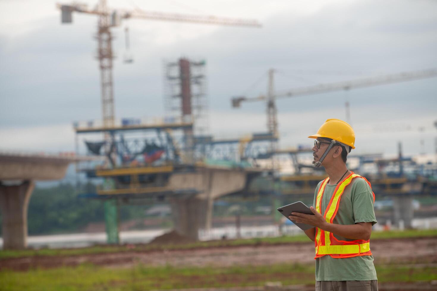 A man in a safety vest is standing in front of a large construction site photo