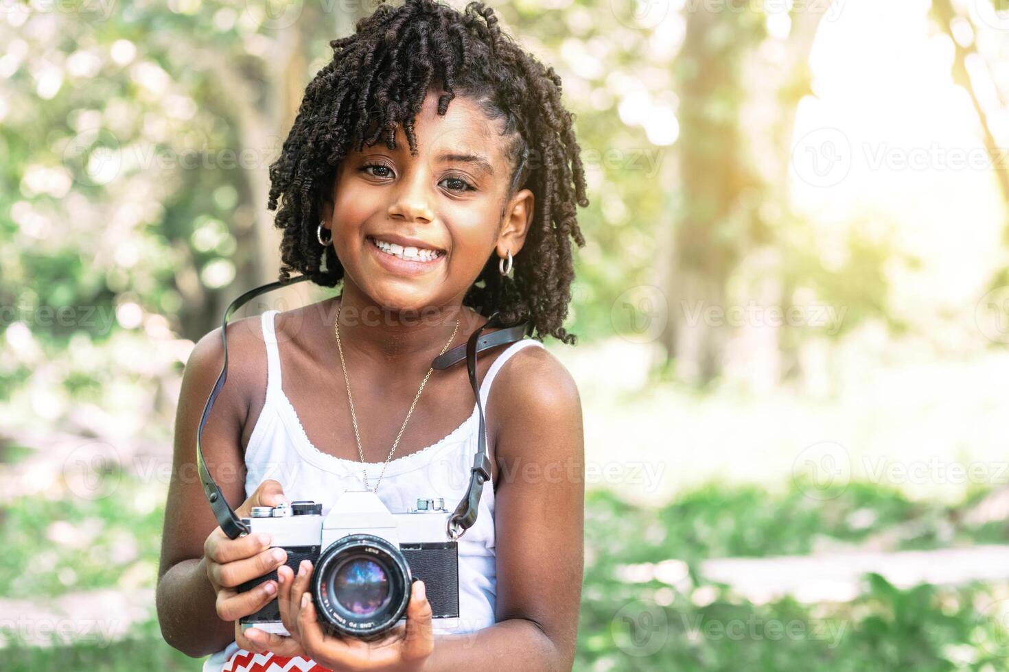 young african american toddler girl holding an old camera and looking at camera. photo