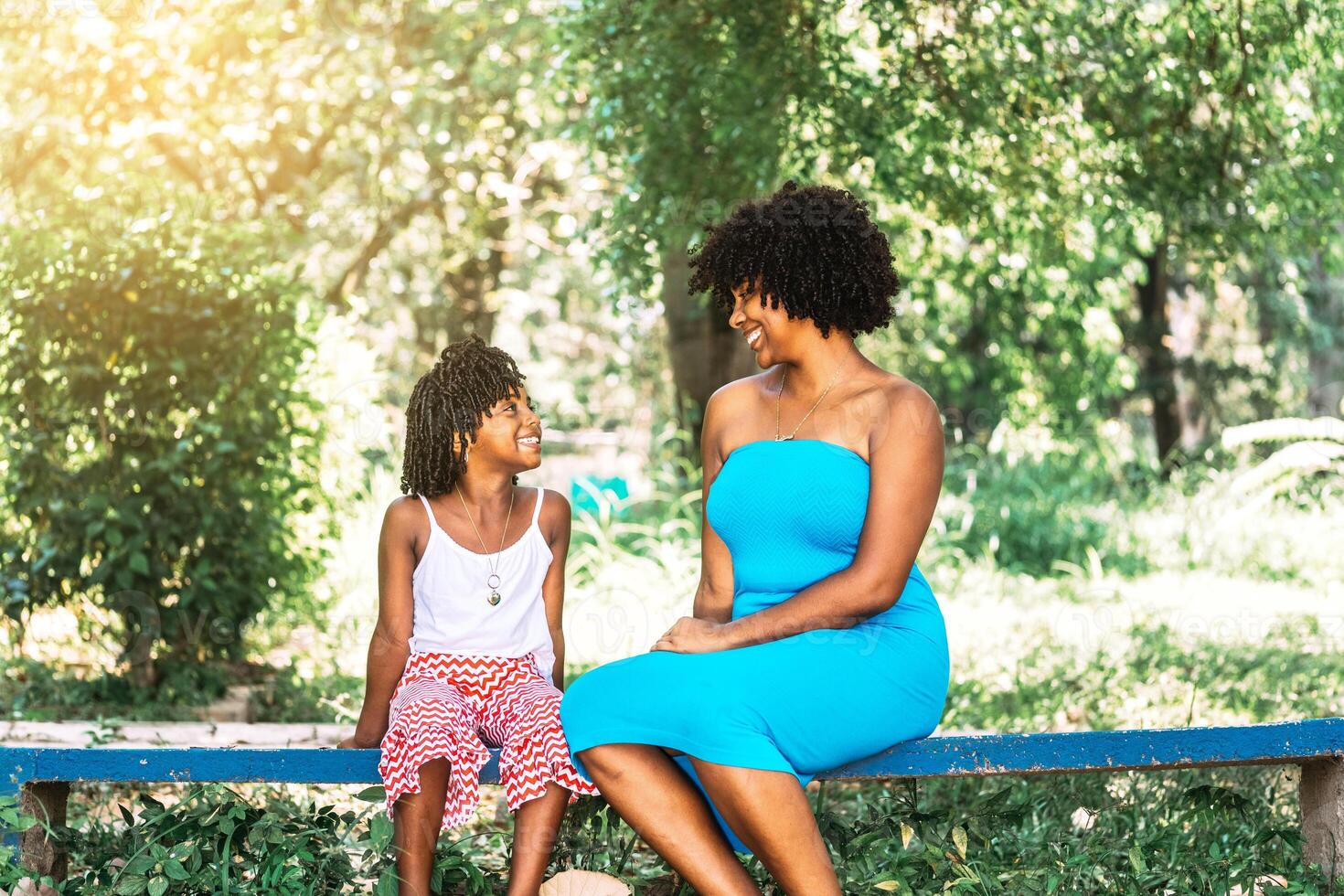 mother and daughter of African American ethnicity sitting in a park looking at each other and talking, smiling and happy. photo
