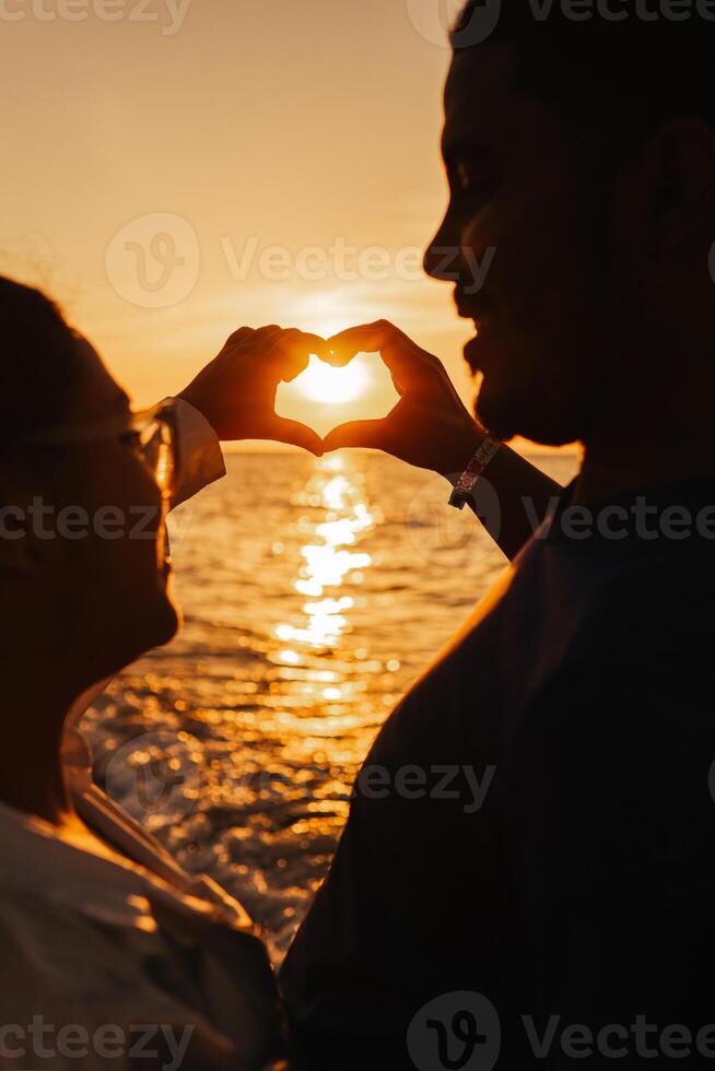 Couple of hetereosexual making a silhouette of the heart of gesture of hands. photo