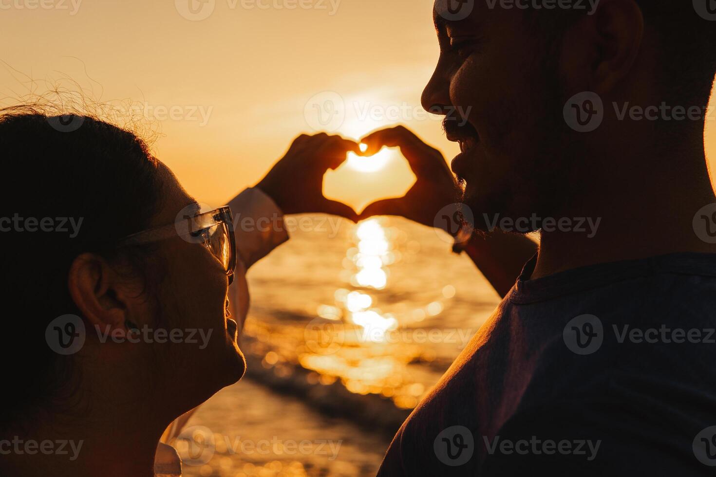 Couple of hetereosexual making a silhouette of the heart of gesture of hands. photo