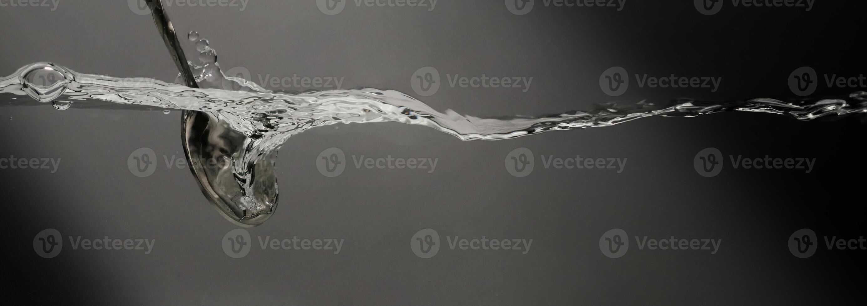 Stirring drinks by bar spoon. Underwater of silver metal bar spoon stir clear alcoholic drinks such as Vodka Gin or Tequila close up shot. Bartender spoon under clear water against grey background. photo