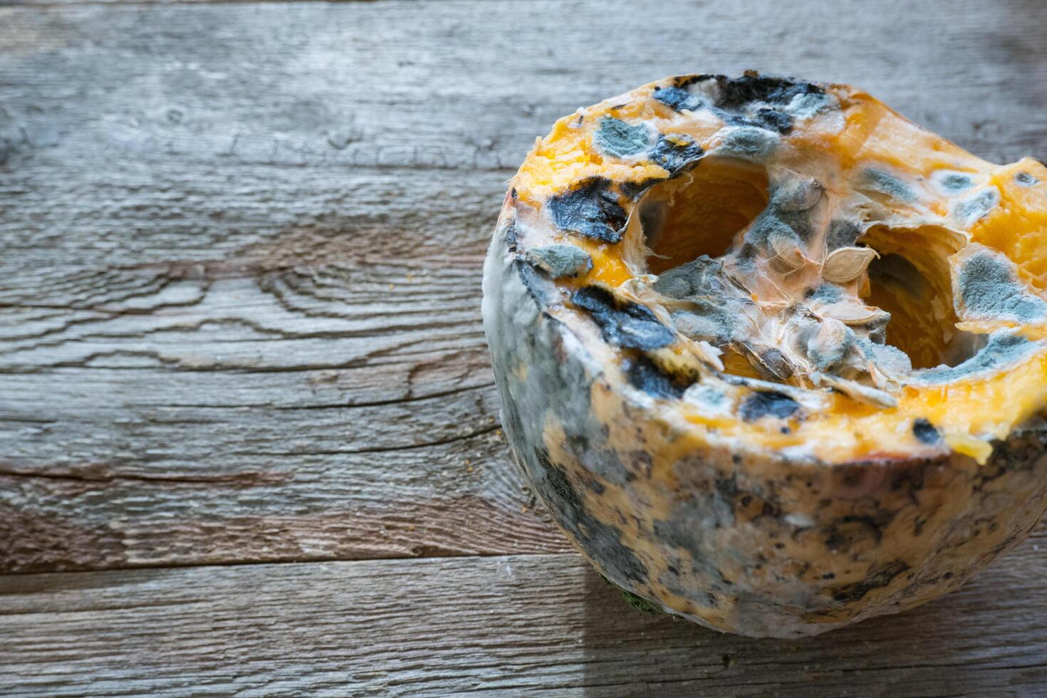 Orange moldy pumpkin on a wooden background. Mold and fungi on food, mold development, pests of stored vegetable products, a common problem. photo