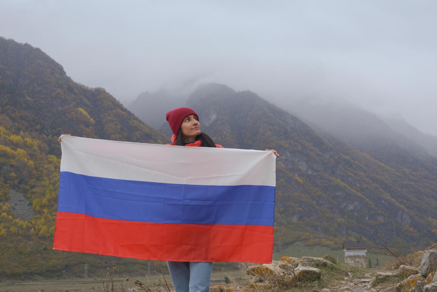 Close-up of the Russian flag fluttering beautifully in the hands of a woman against the backdrop of the Caucasus Mountains on a cloudy foggy day. Russian Independence Day photo