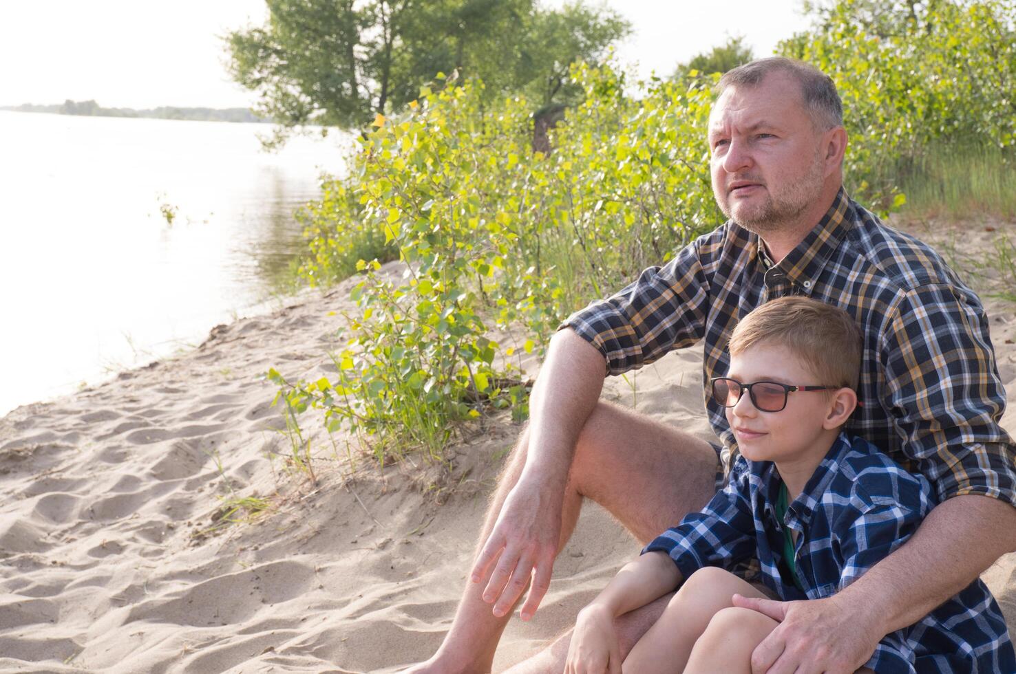 Father's day concept. Father and son sit together on the river bank and look into the distance. photo