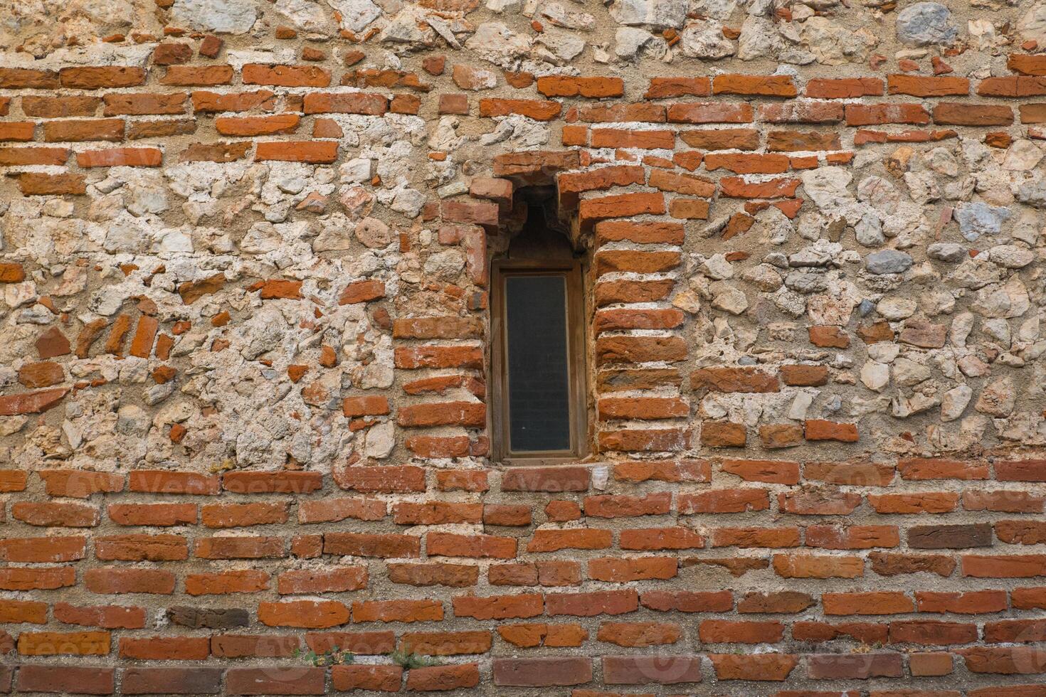 An arched window in a fortress or castle made of red stone. Architecture of old stone buildings. Window in the wall. Window with an arch of an old castle. photo