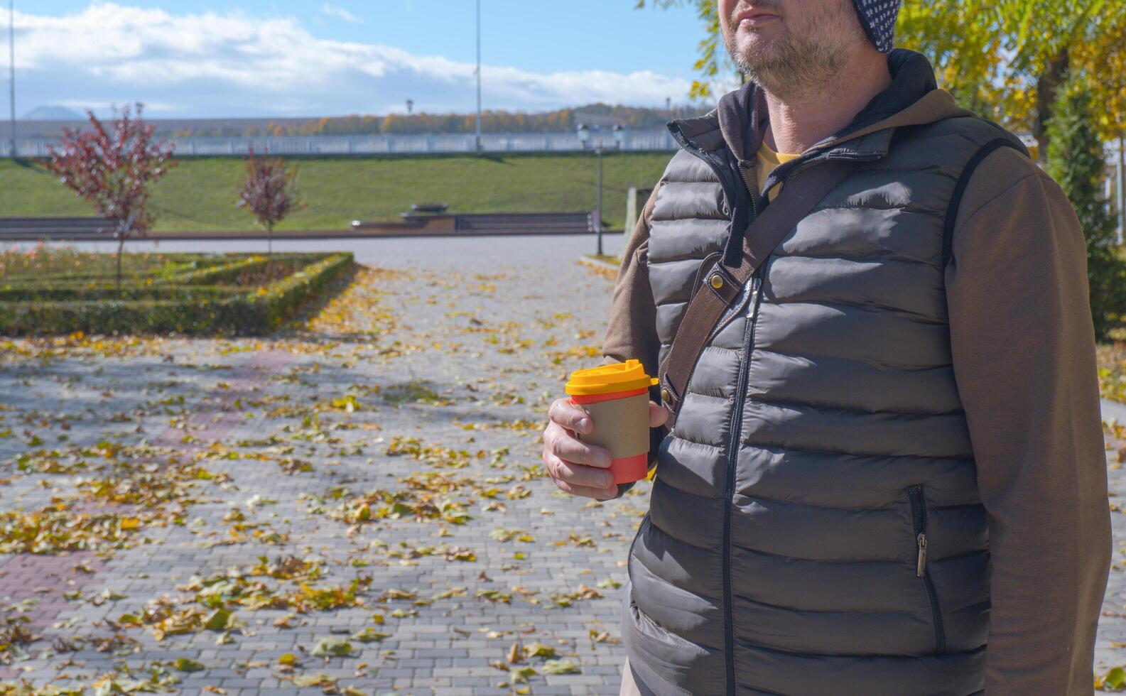 A young man walks in an autumn park and drinks coffee, rests, relaxes. Urban lifestyle concept. photo