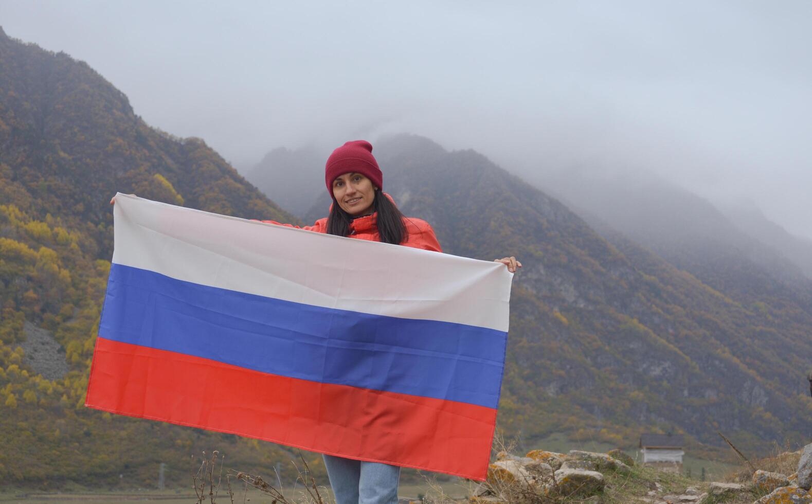Close-up of the Russian flag fluttering beautifully in the hands of a woman against the backdrop of the Caucasus Mountains on a cloudy foggy day. Russian Independence Day photo