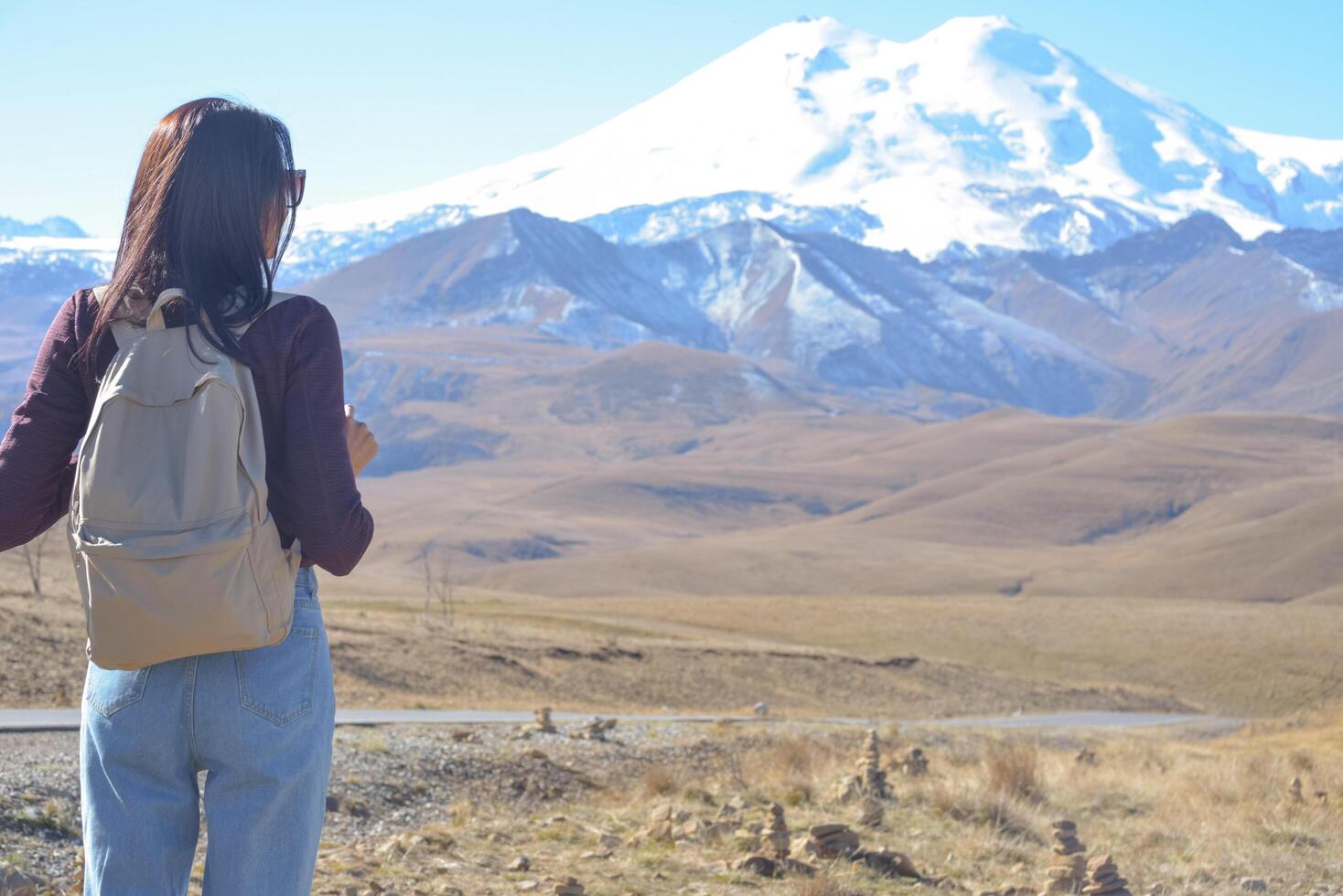 A female traveler with a backpack on her back admires the snow-covered Elbrus on a clear autumn day. View of Elbrus, North Caucasus, Russia photo