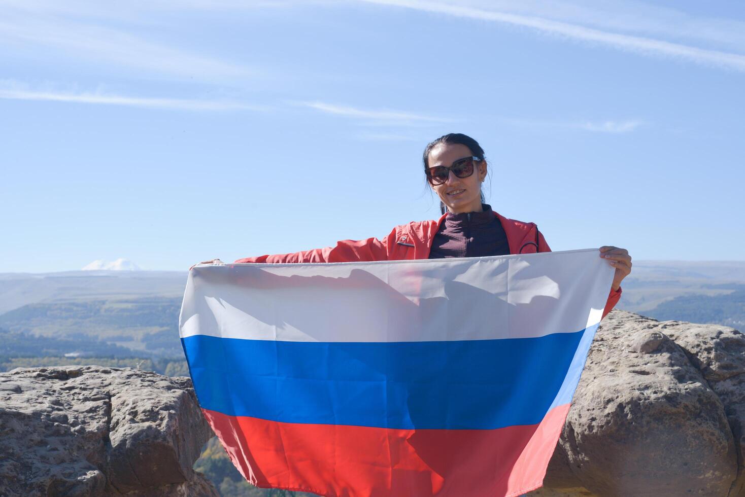 The Russian flag is on the shoulders of a girl standing against the backdrop of the Caucasus mountains. Unity Day in Russia. photo