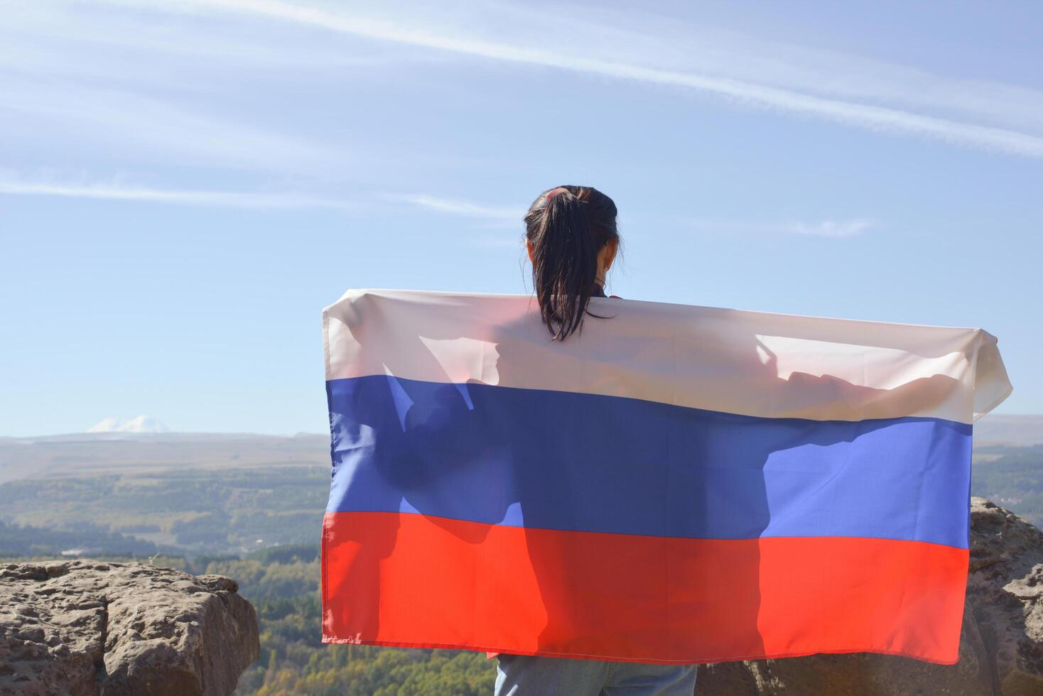 The Russian flag is on the shoulders of a girl standing against the backdrop of the Caucasus mountains. Unity Day in Russia. photo