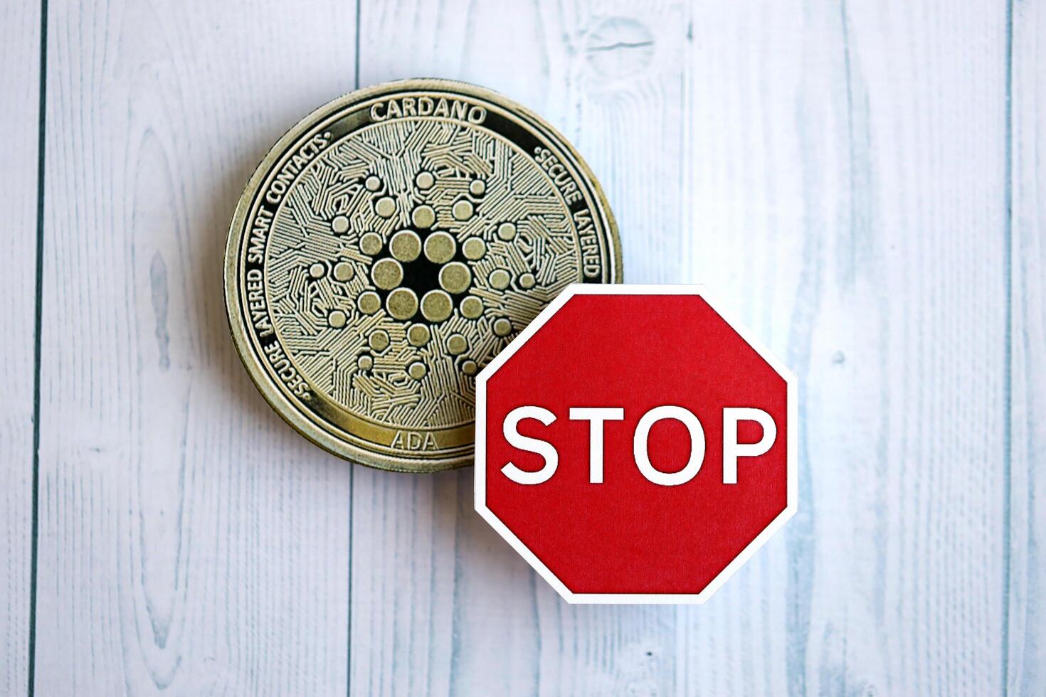 KYIV, UKRAINE - AUGUST 17, 2024 Cardano ADA coin and red paper stop sign on wooden background photo
