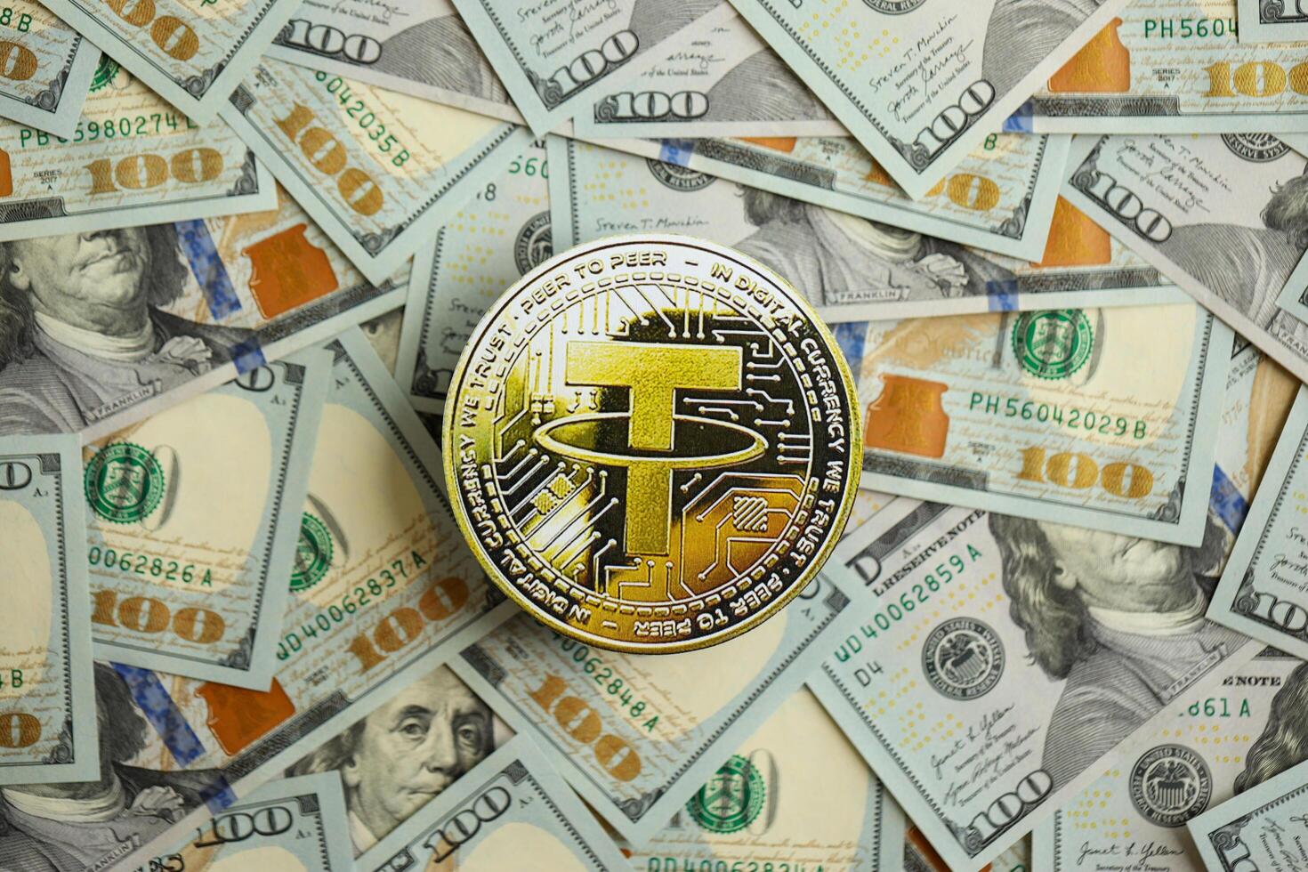 KYIV, UKRAINE - AUGUST 17, 2024 Tether USDT coin on big amount of hundred US dollar bills photo