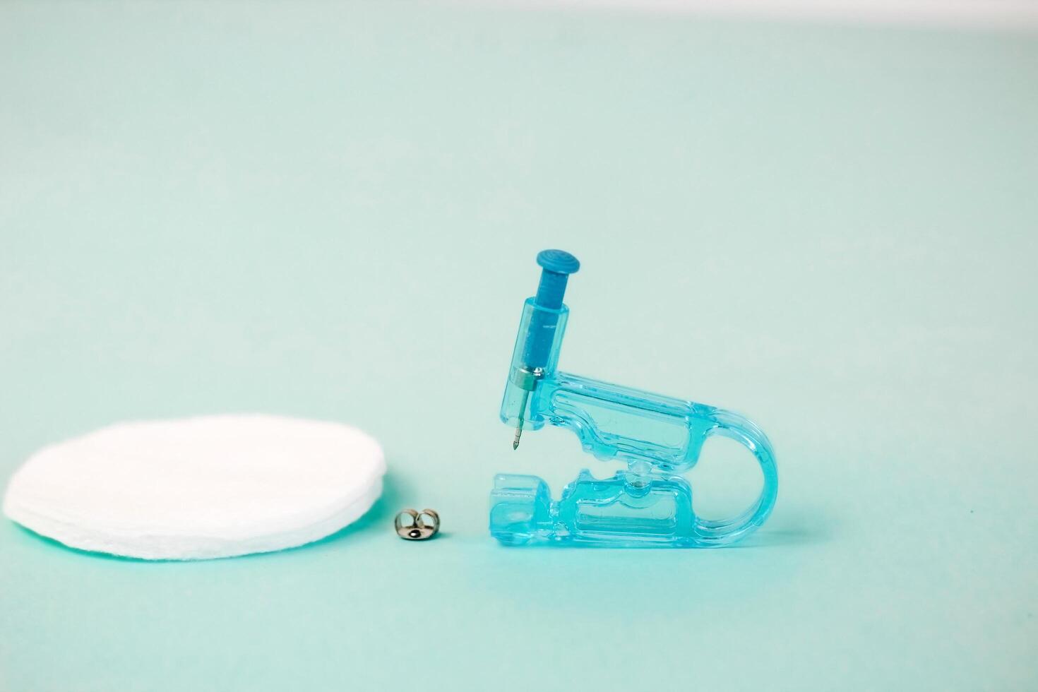 Disposable plastic gun for earrings on a turquoise background. Safe piercing photo