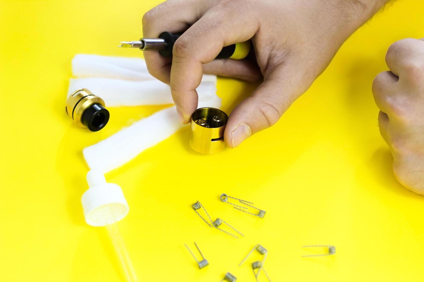 electronic cigarette details, Vata, coils, drip, spring, nippers on a yellow background. man's hands change springs in vape photo