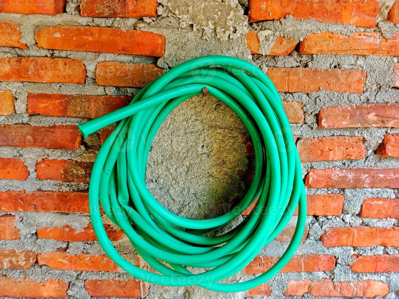 roll of green rubber water hose hangs on a brick wall photo