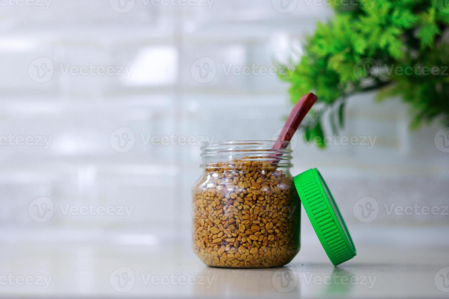 Fenugreek seeds in a plastic jar with green leaves on a white background photo