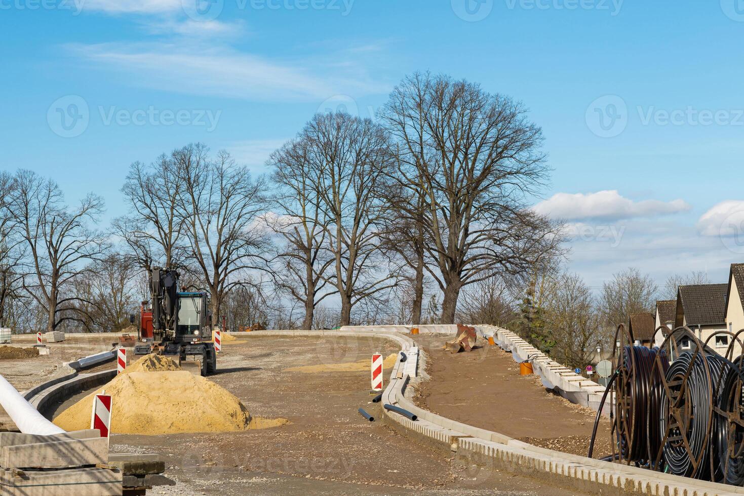Construction site for laying the road surface with an excavator standing on it and a pile of sand in front. photo