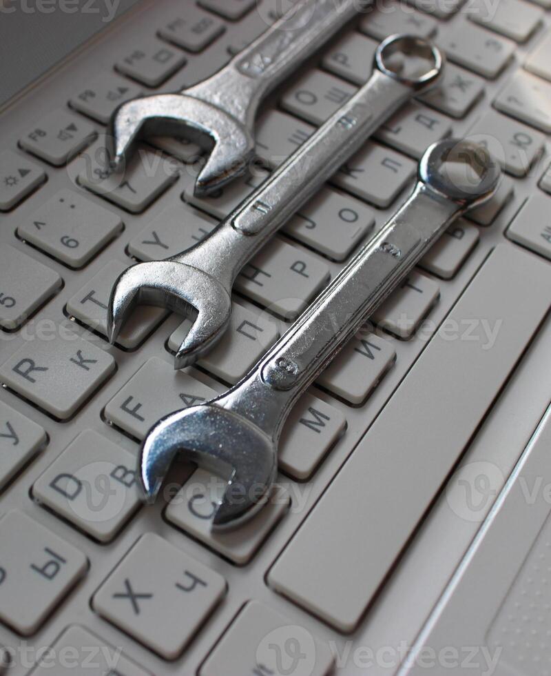 Metallic wrenches on a buttons of laptop keyboard vertical stock photo. Different types of hardware concept image photo
