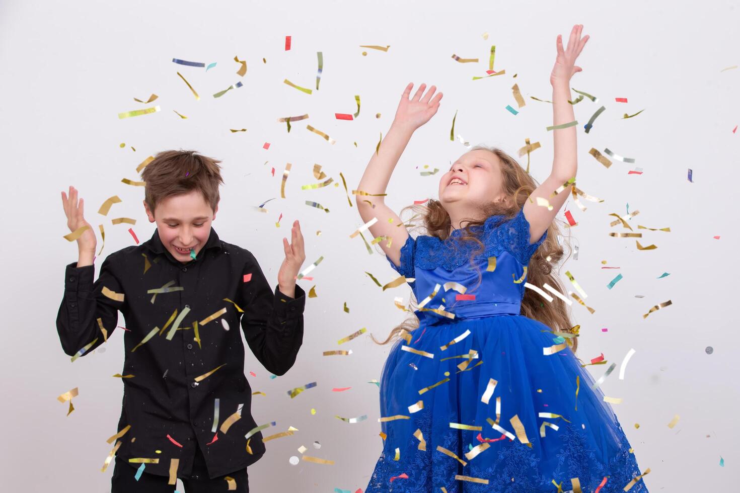 Happy party. Small handsome boy and his little pretty sister wearing cone caps laughing and throwing colorful confetti isolated on white background photo