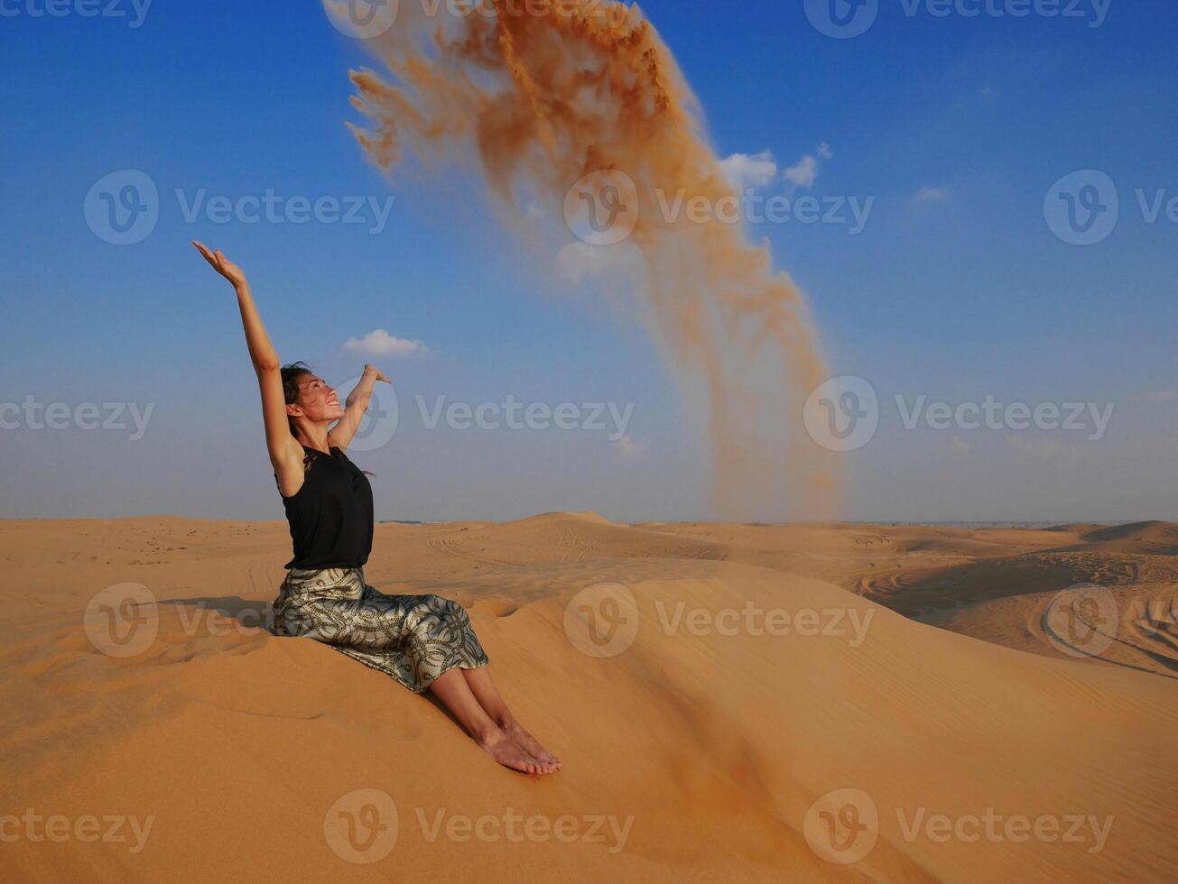 A girl in the Dubai desert throws sand up and smiles photo