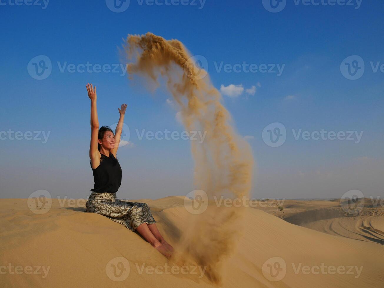 A girl in the Dubai desert throws sand up and smiles photo