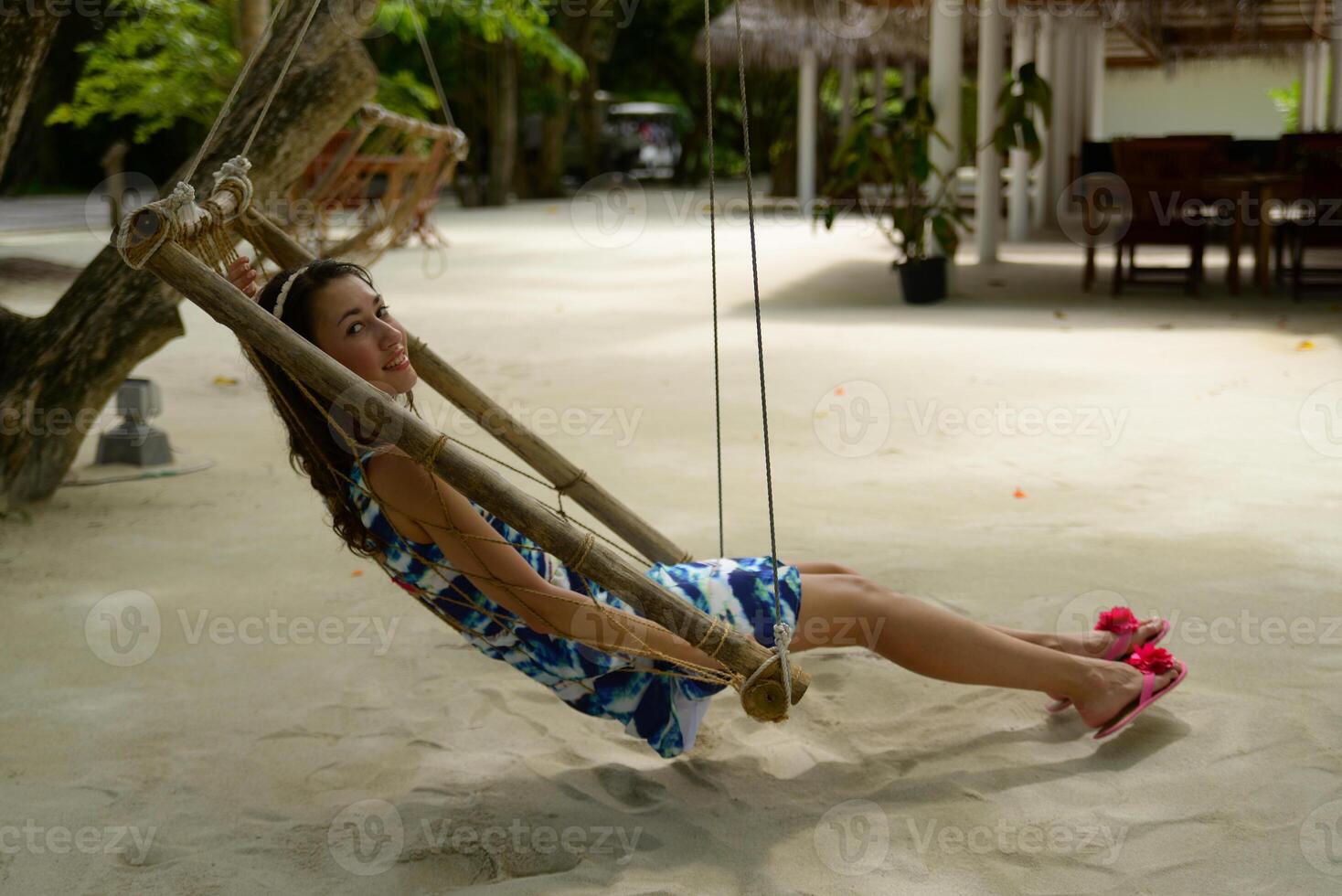 A smiling girl wearing dress sits in a hammock on a tropical beach photo