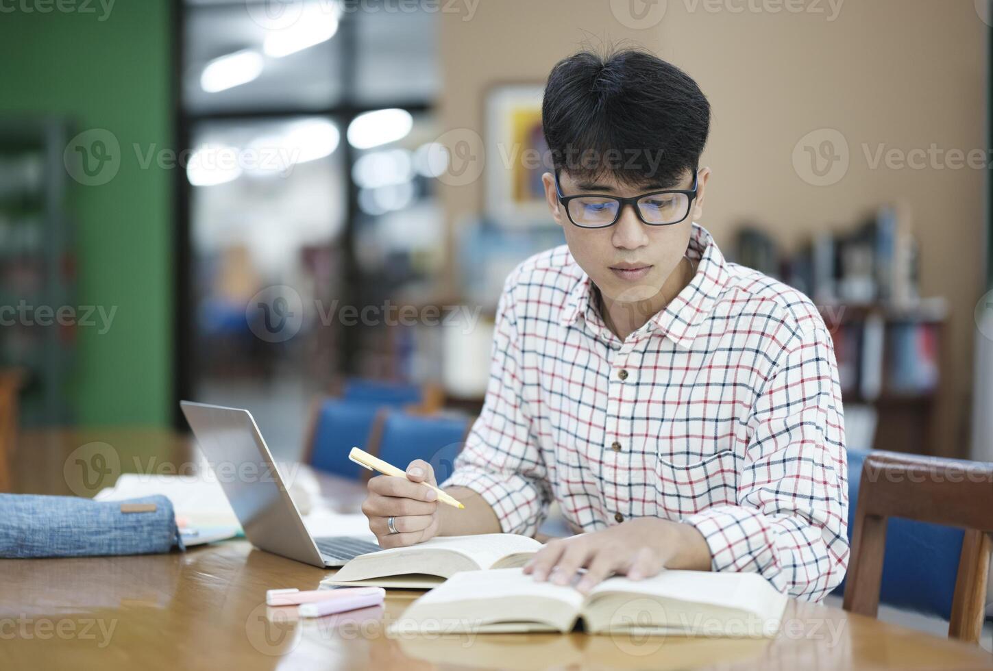 Young Asian male sitting inside a library alone doing research. Man working on a project. Young man doing research for a case. photo