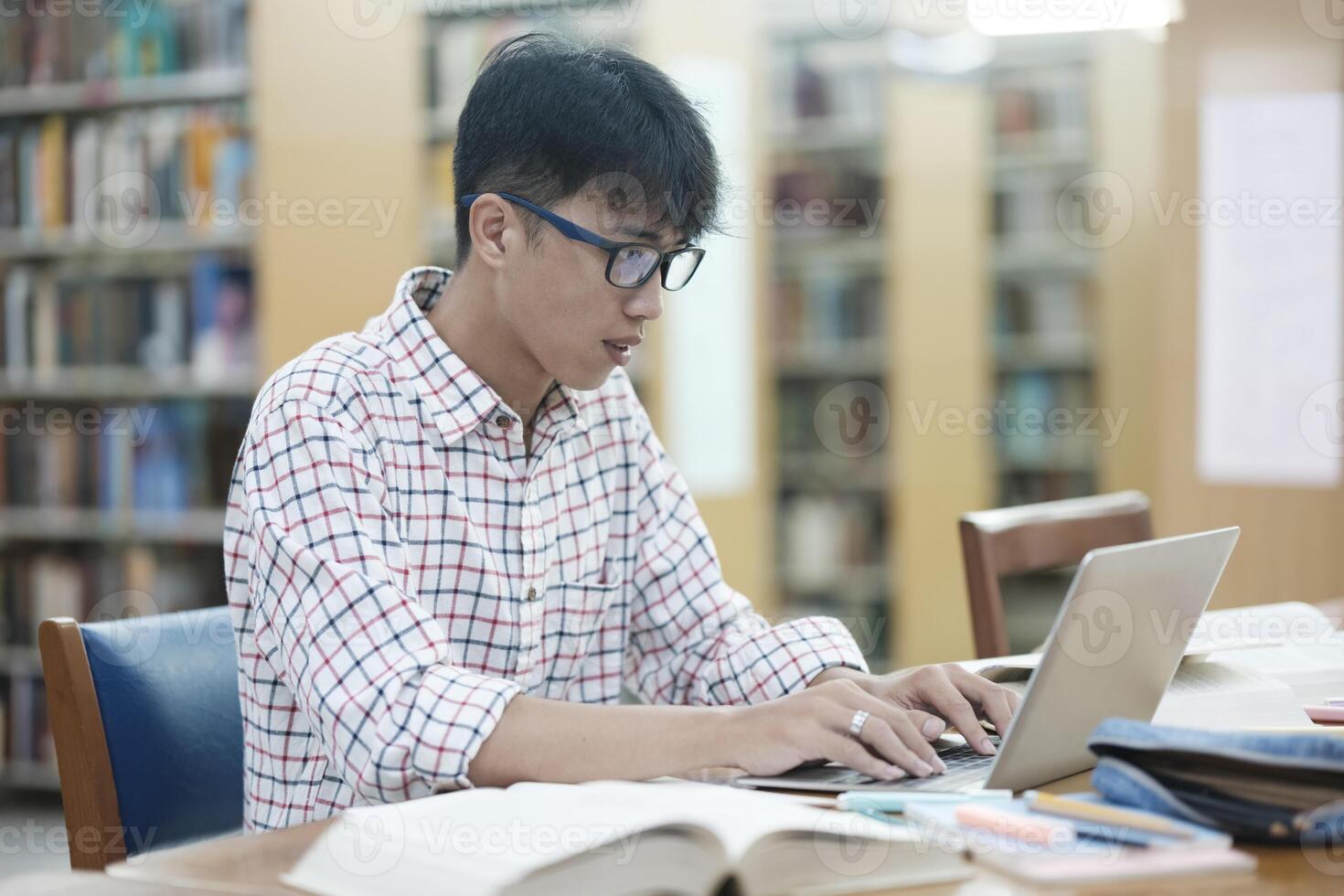 Young Asian male sitting inside a library alone doing research. Man working on a project. Young man doing research for a case. photo