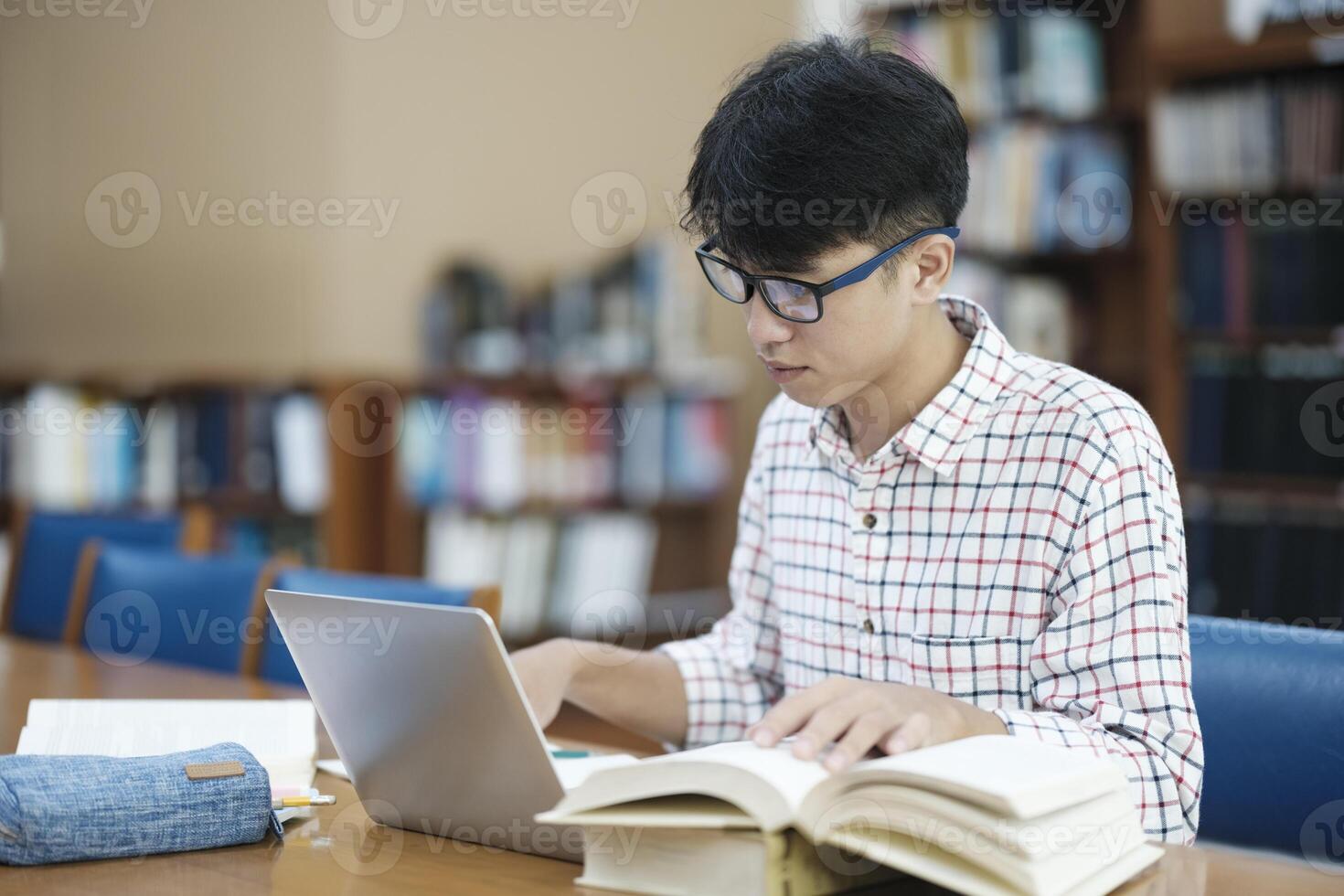 Young Asian male sitting inside a library alone doing research. Man working on a project. Young man doing research for a case. photo