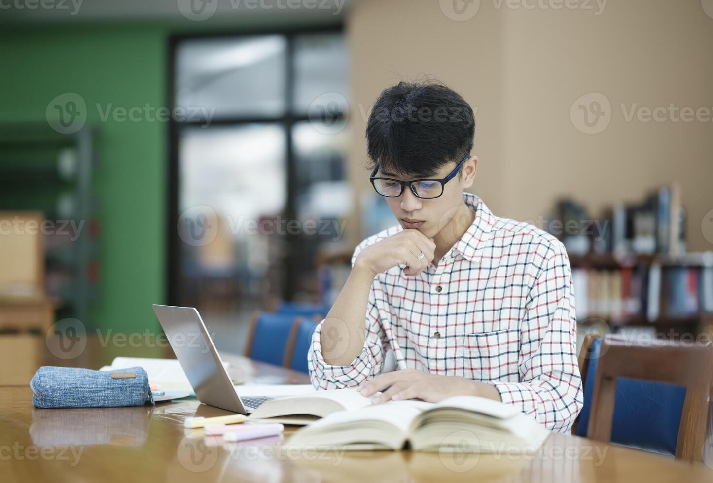 Young Asian male sitting inside a library alone doing research. Man working on a project. Young man doing research for a case. photo