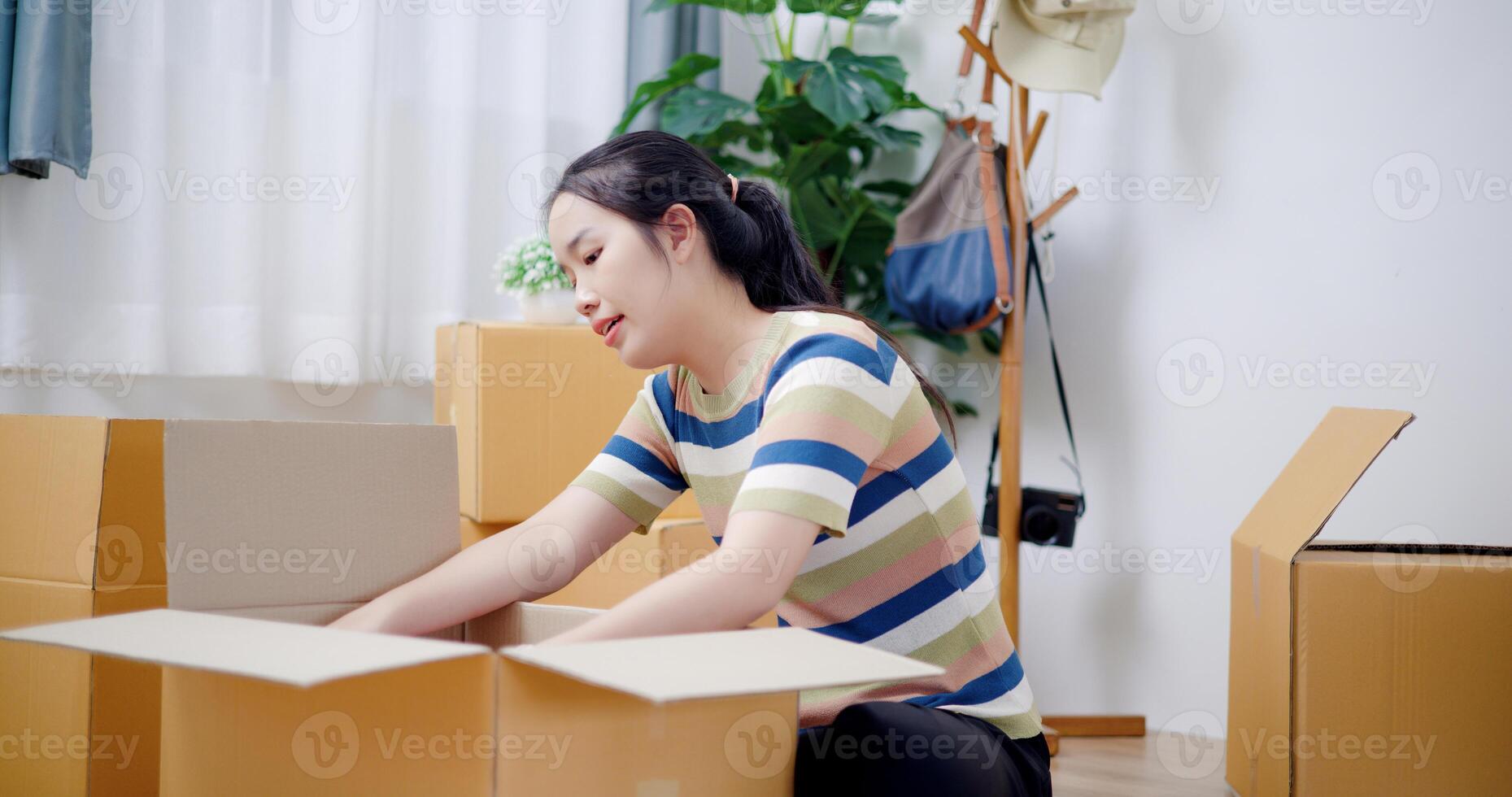 Portrait of Happy young woman packing her things into a cardboard box in preparation for moving to a new house. Moving and lifestyle concepts. photo