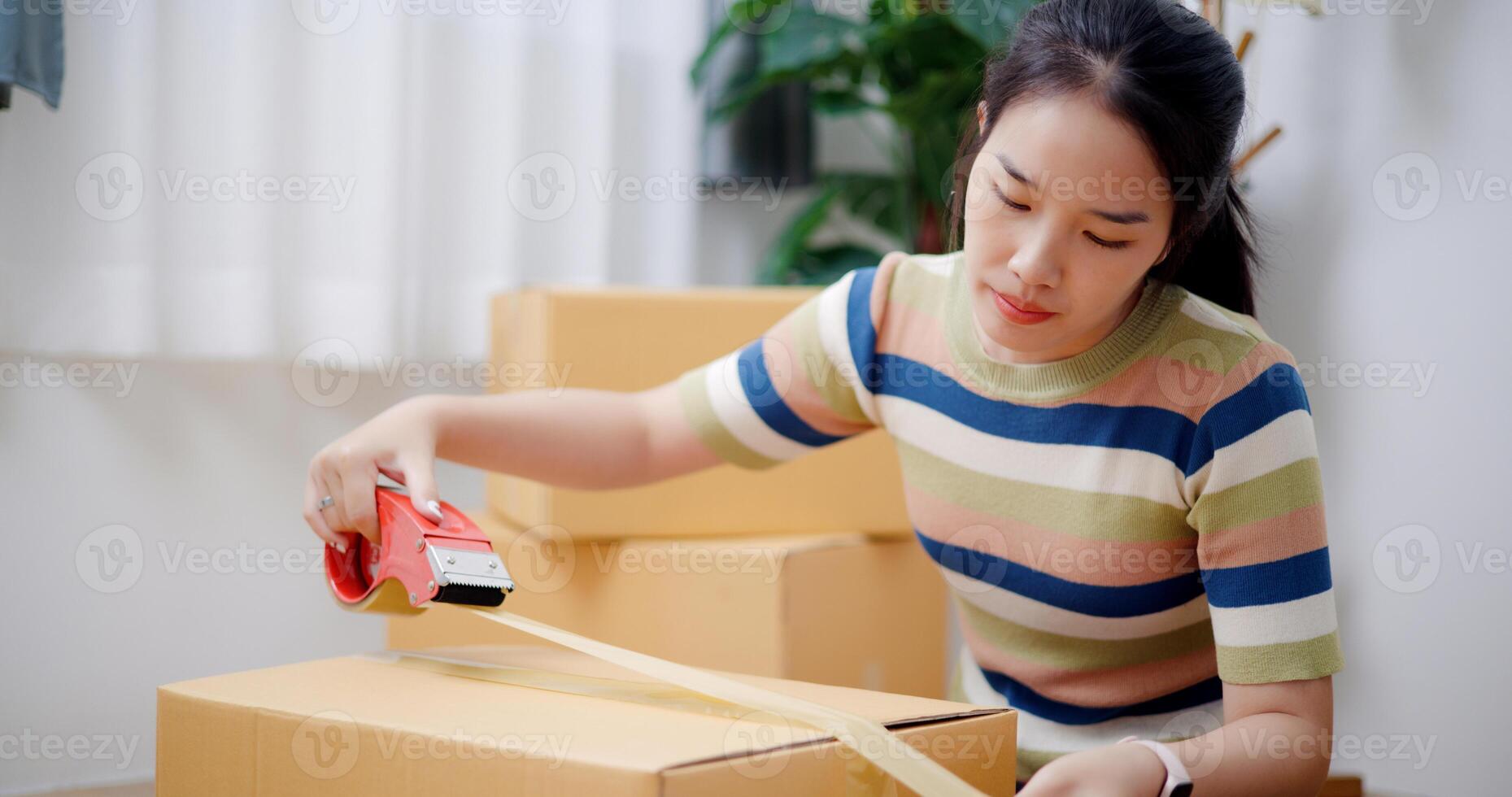 Selective focus, Young Asian woman wrapping cardboard boxes with duct tape in preparation for moving into new house. Moving house and lifestyle concept. photo