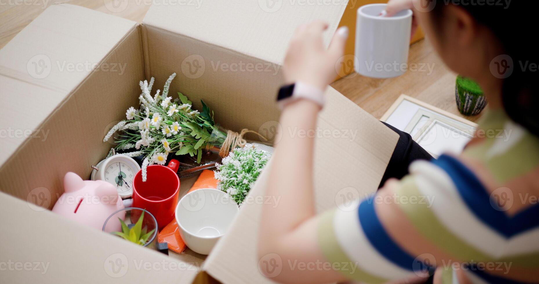 High angle view, Young Asian woman unpacking cardboard boxes and removing items to prepare for new house decoration. Moving house and lifestyle concept. photo