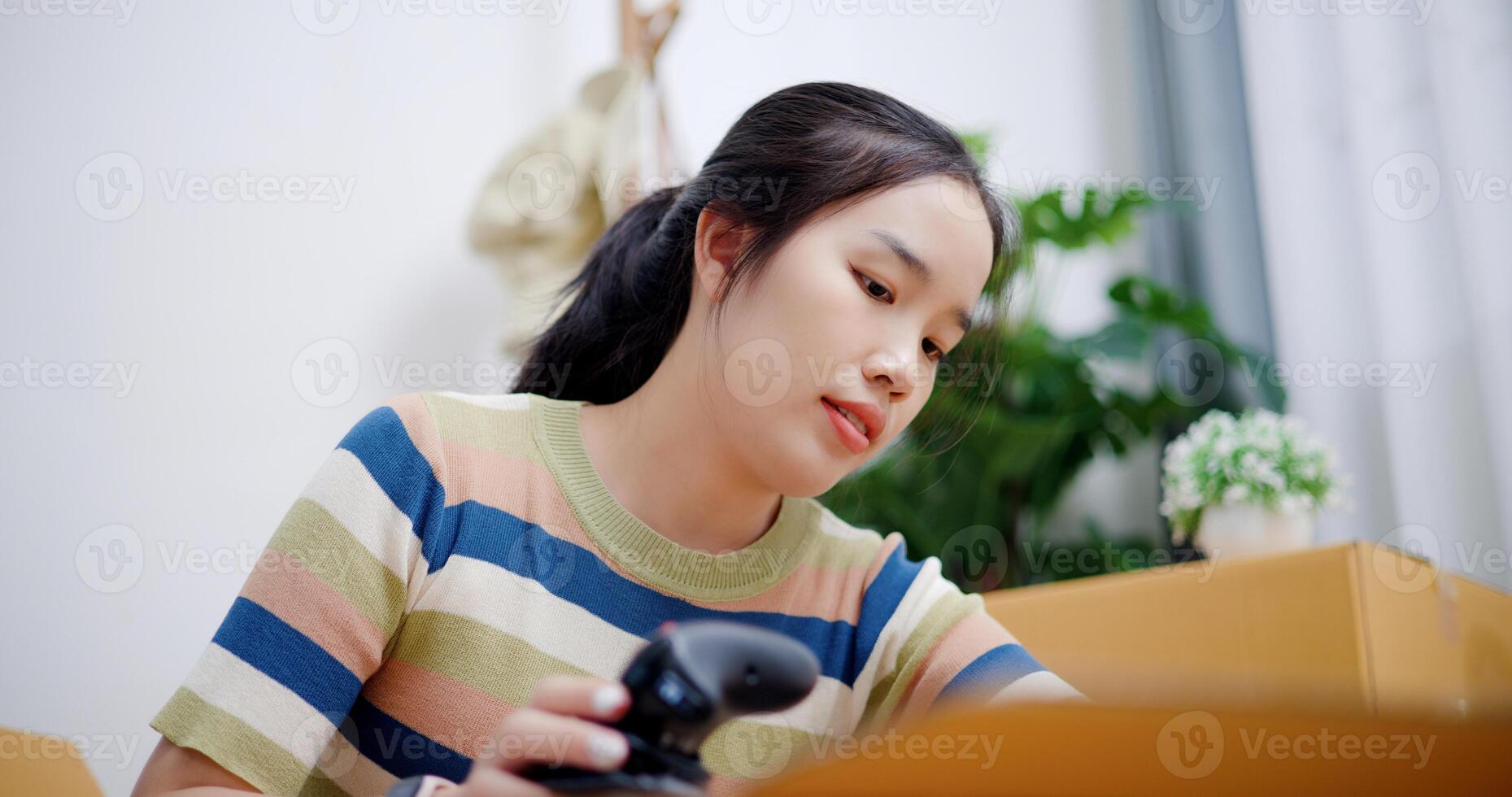 Portrait of Young Asian woman unpacking cardboard boxes and removing items to prepare for new house decoration. Moving house and lifestyle concept. photo
