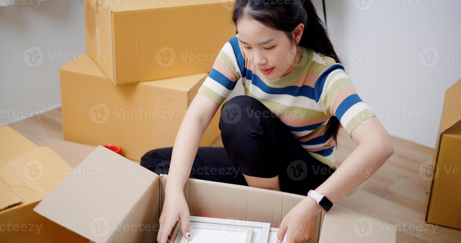 High angle view, Young Asian woman unpacking cardboard boxes and removing items to prepare for new house decoration. Moving house and lifestyle concept. photo