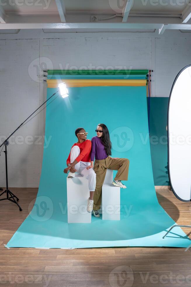 Two women pose on a color background cyclorama in a studio photo shoot.