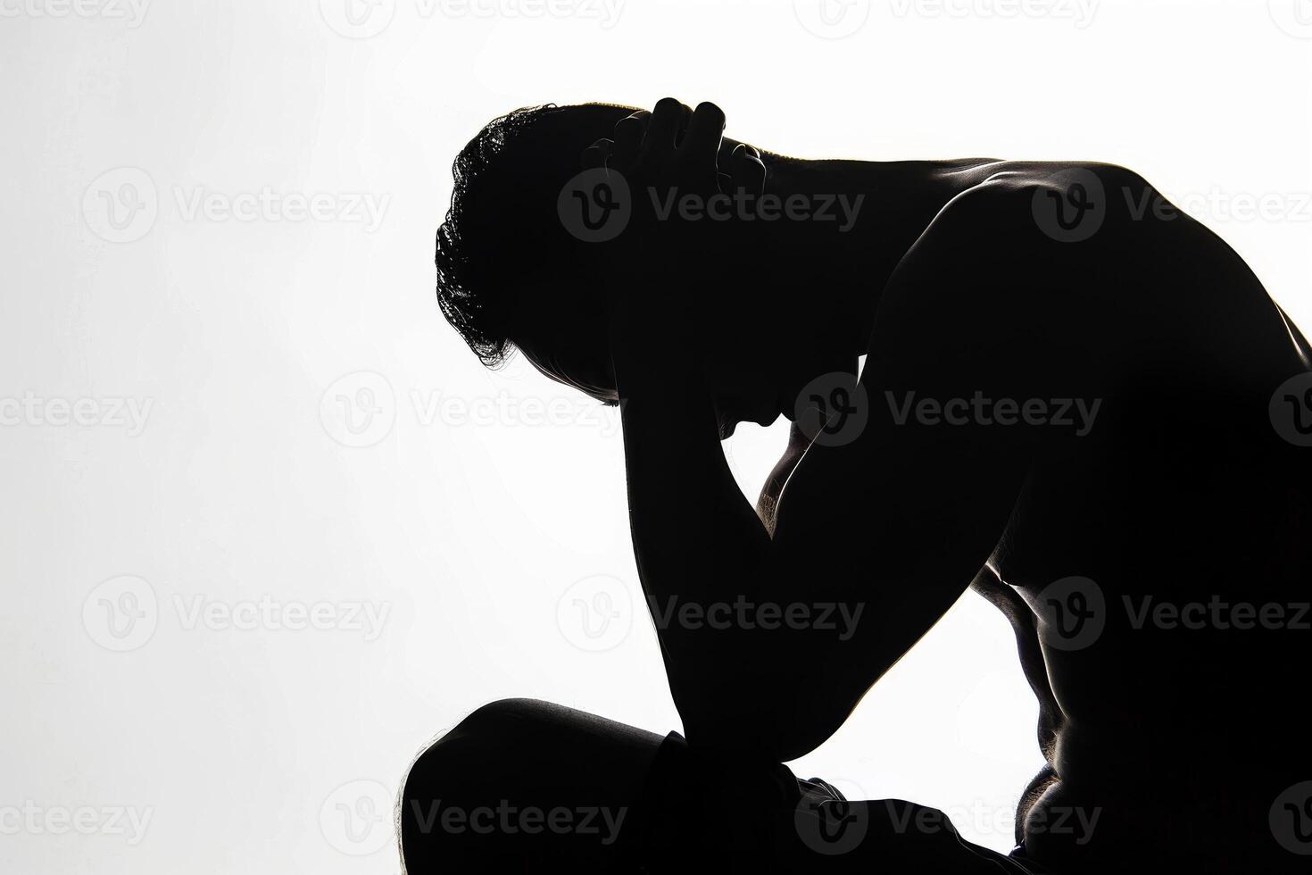 Silhouette of a man sitting with his head down on his hands, expressing suffering photo