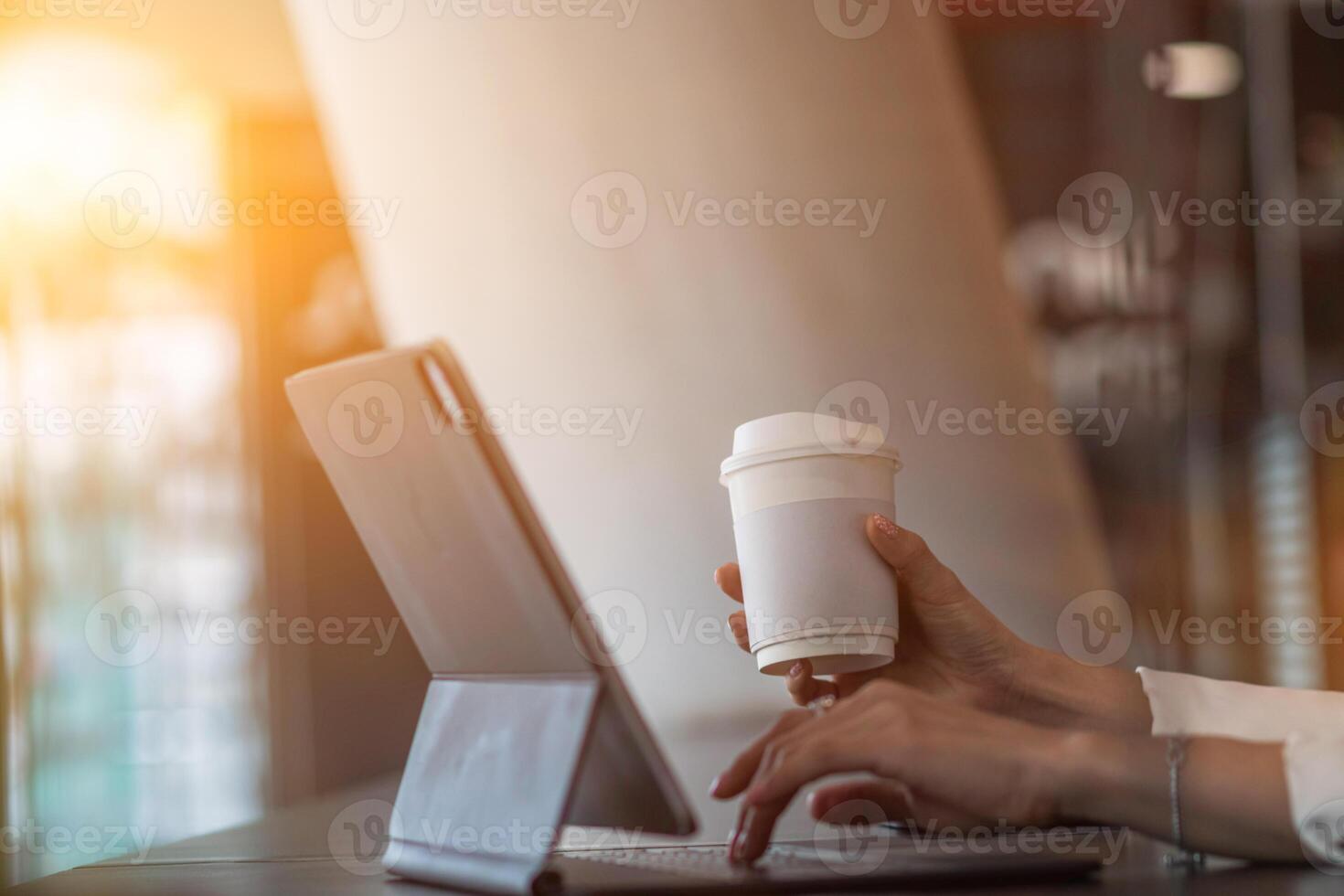 An Asian businesswoman holds a cup of coffee in her hand and drank while checking her computer online as she is starting a business that can order and check from anywhere online. photo