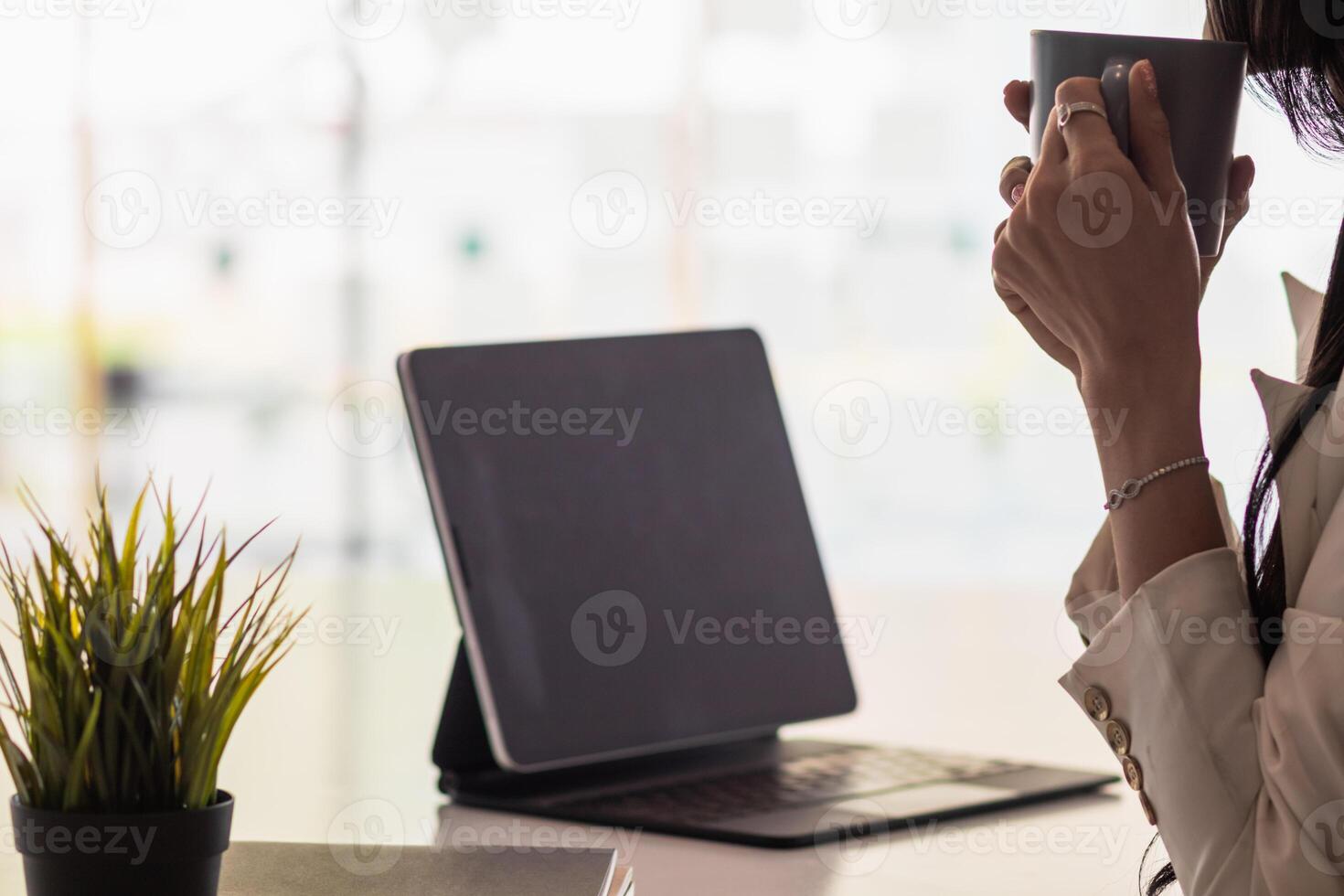 An Asian businesswoman holds a cup of coffee in her hand and drank while checking her computer online as she is starting a business that can order and check from anywhere online. photo