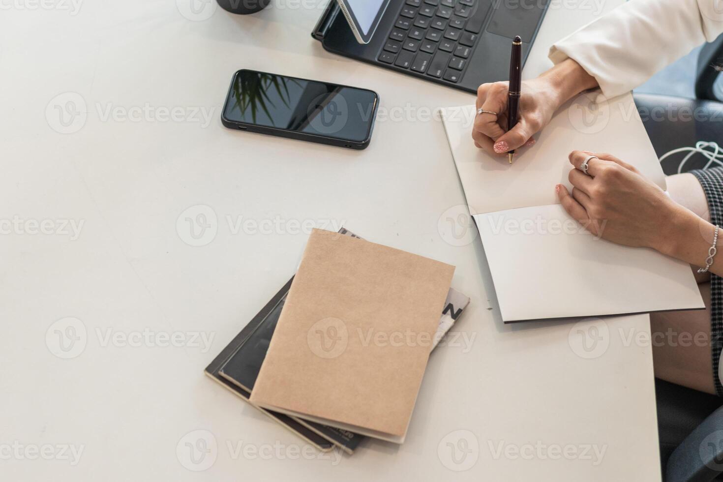 A businesswoman sits at her desk in her office and uses a pen to jot down appointments in her notebook as a reminder. Notebooks are still popular for note taking and are used a lot in school. photo