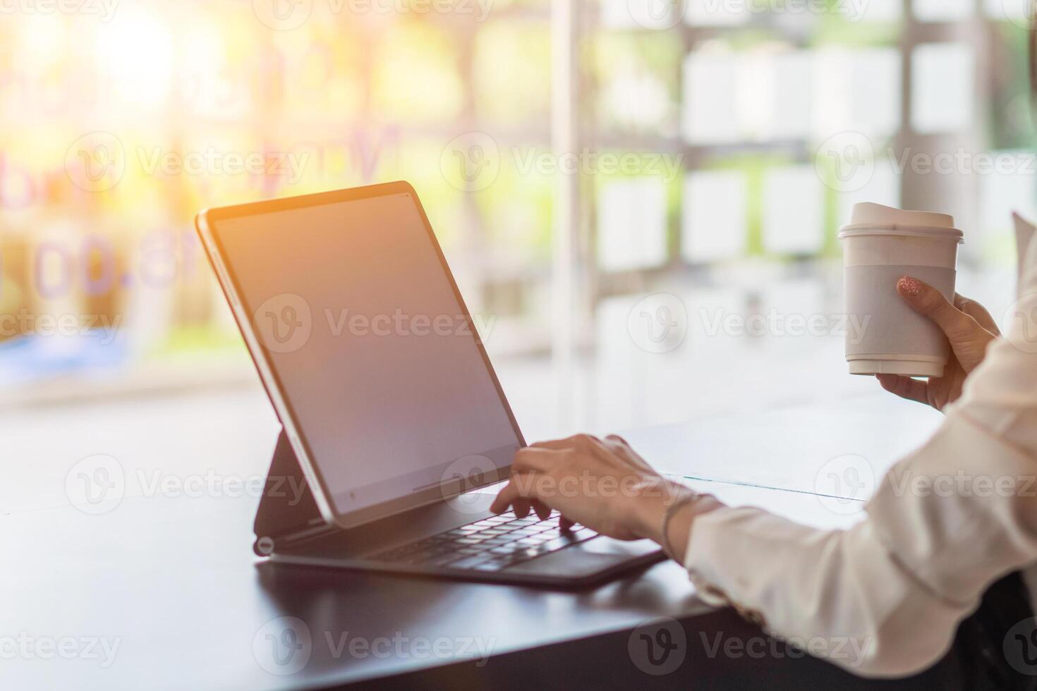An Asian businesswoman holds a cup of coffee in her hand and drank while checking her computer online as she is starting a business that can order and check from anywhere online. photo