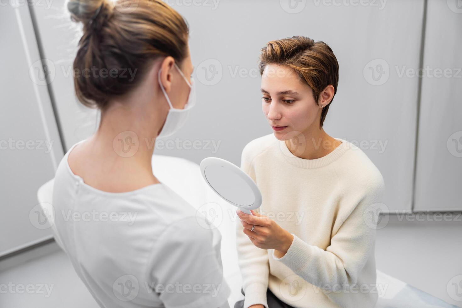 Woman consulting with a professional while examining her reflection in a mirror at a clinic photo