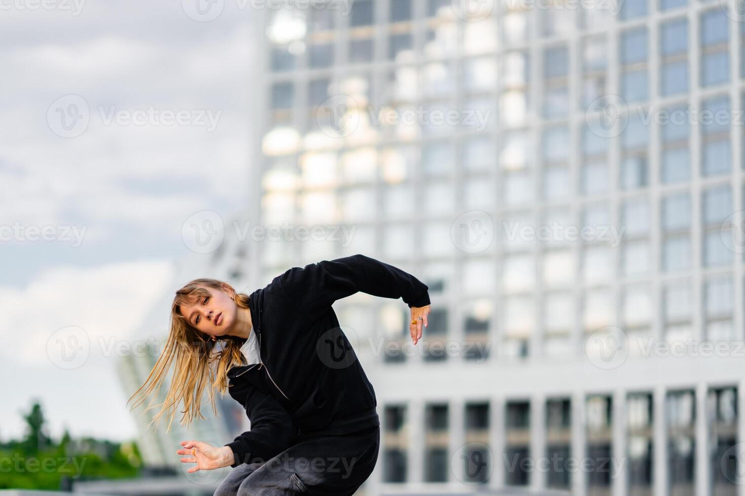 Young Dancer Performing Urban Dance Routine at Modern Cityscape During Overcast Afternoon photo