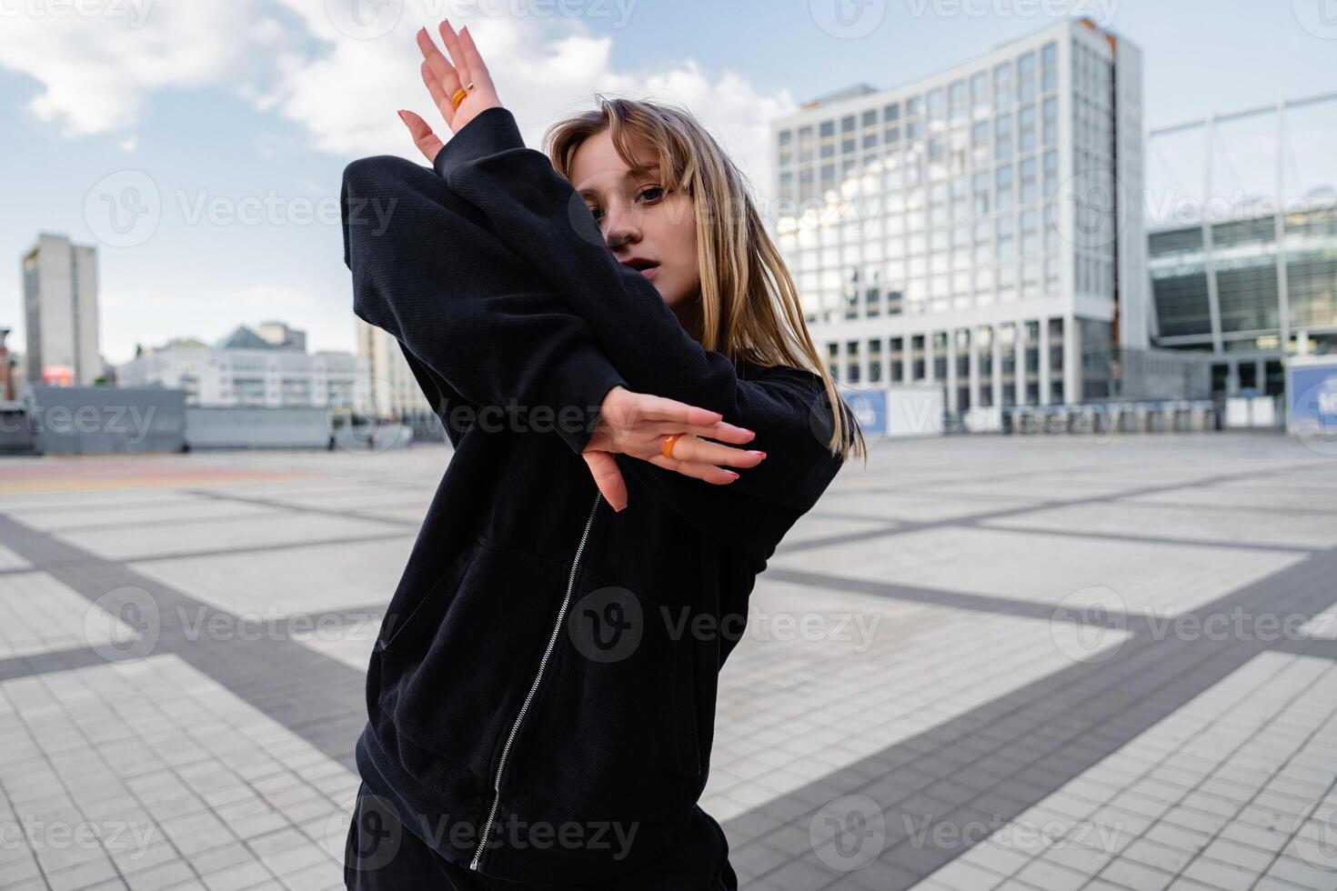 Young Woman Performing Dance Moves in Urban Setting During Daytime at a Modern City Square photo