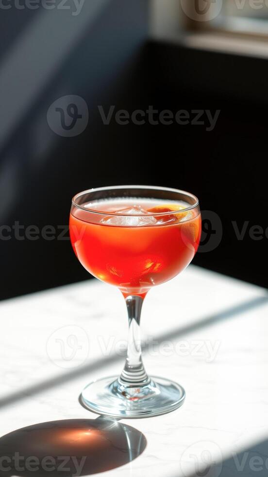 Red Cocktail with Ice and Orange Slice in a Glass on White Marble photo