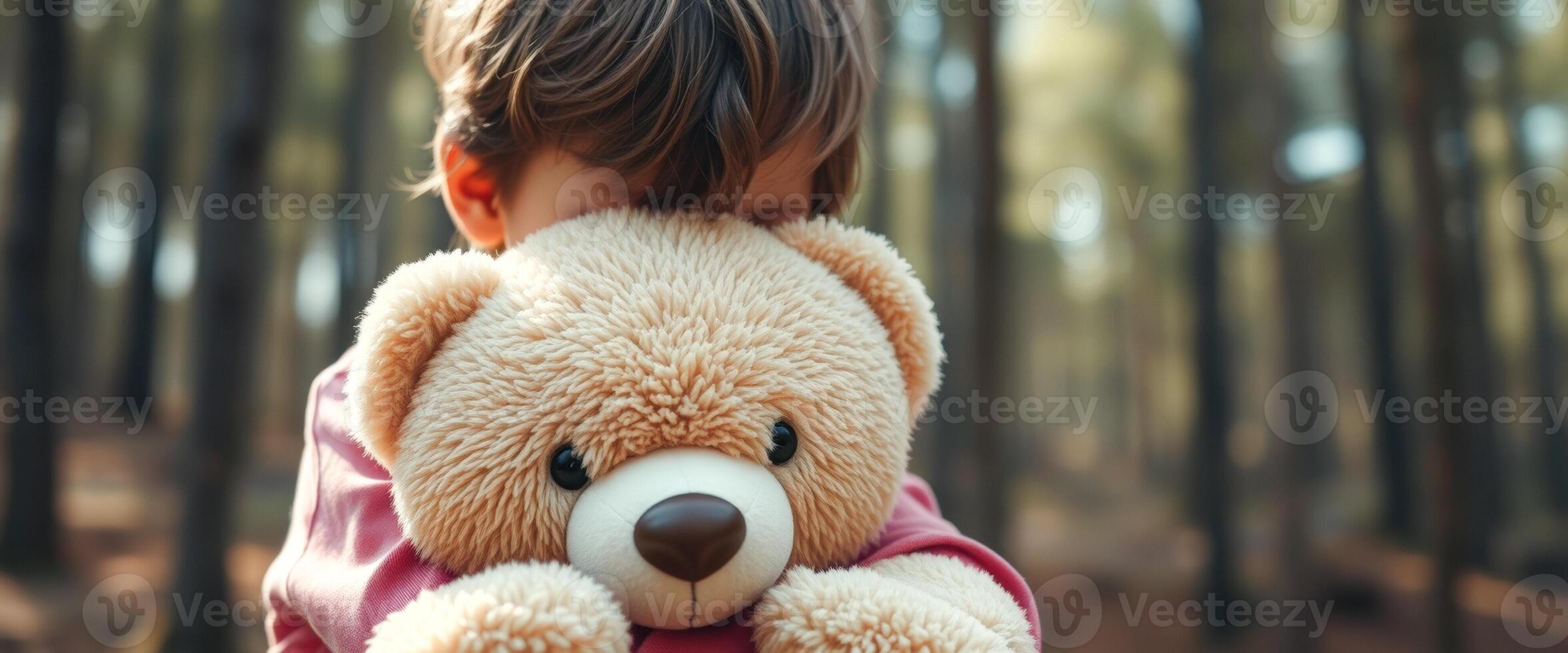 Child hugging teddy bear in forest photo
