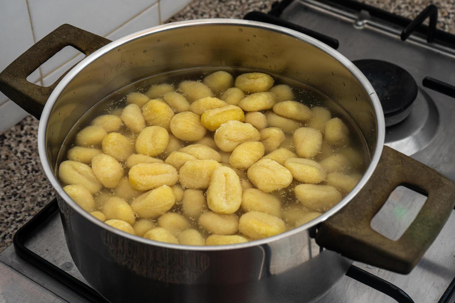 A pan of gnocchi simmering over a flame on a stovetop in a traditional restaurant kitchen, with golden pieces gently cooking in the rustic setting. photo