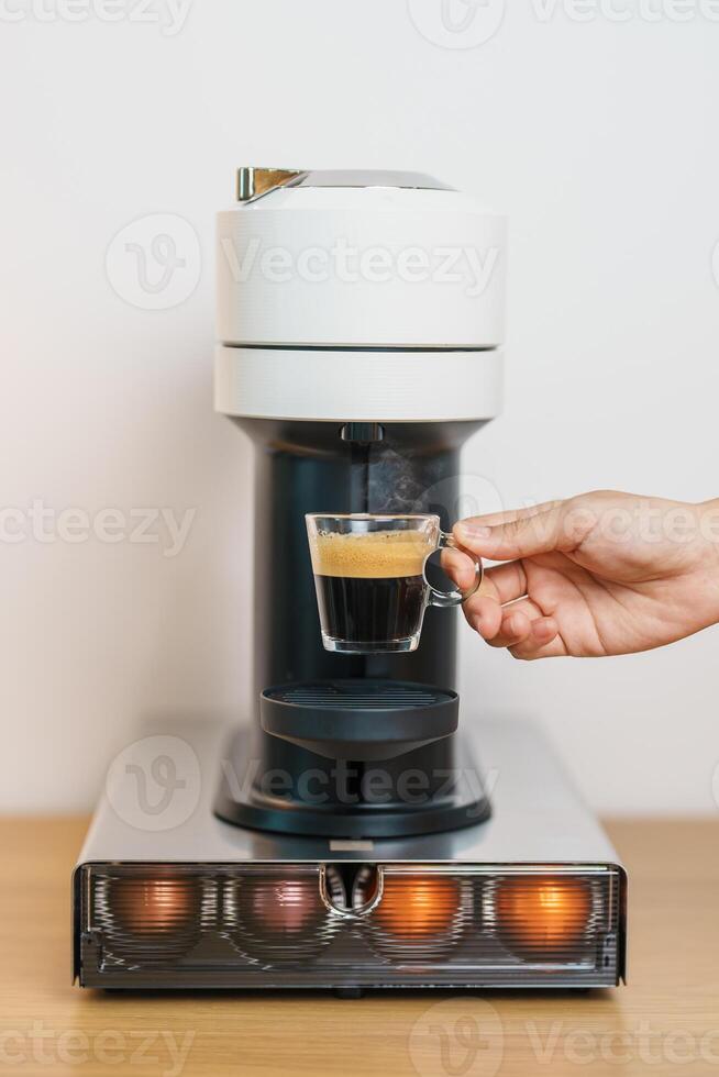 hand making Espresso Coffee by Coffee Maker Machine with Capsule of roasted coffee bean on wood table bar. Daily beverage drink at Home, Apartment and Office concept photo