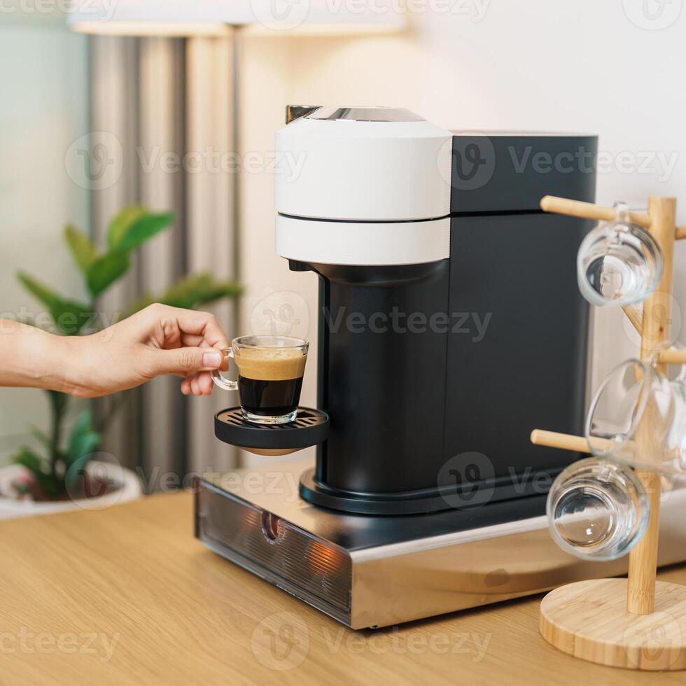 hand making Espresso Coffee by Coffee Maker Machine with Capsule of roasted coffee bean on wood table bar. Daily beverage drink at Home, Apartment and Office concept photo
